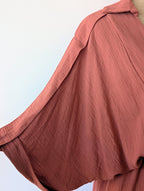 Robe longue terracotta en viscose avec fil dore.  Col chemise et drapé sur le devant. Manches chauves souris.